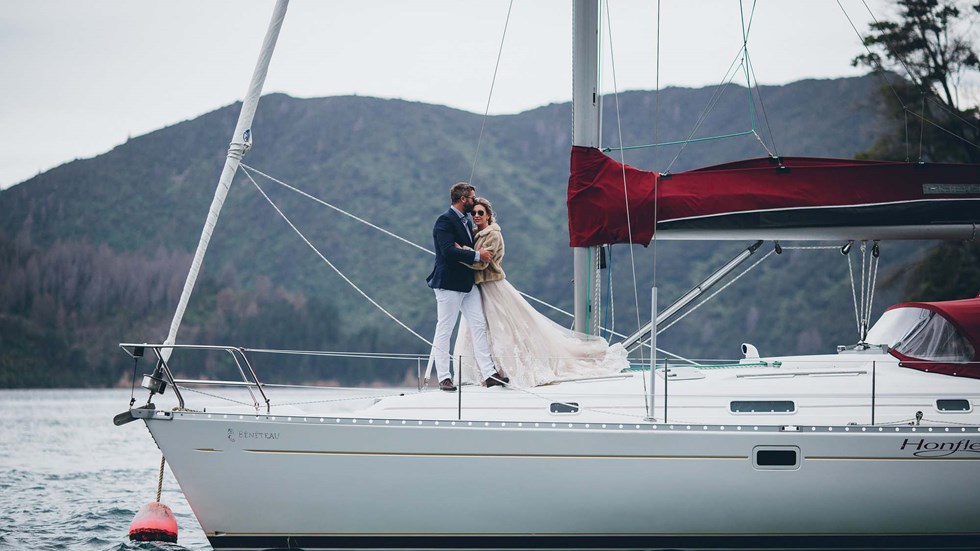 A Bride and Groom embrace on a moored yacht in the Punga Cove bay with Endeavour Inlet scenic views in the Marlborough Sounds of New Zealand