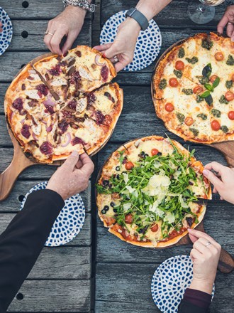 A group of friends share three hot stone baked pizzas and drinks from the Boatshed Cafe and Bar at Punga Cove located in the Marlborough Sounds of New Zealand's South Island