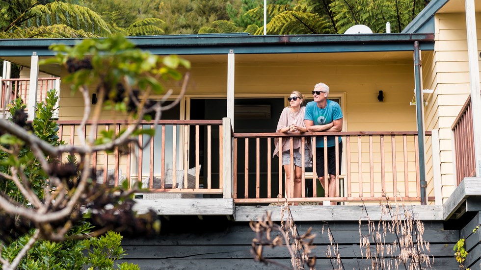 Couple admire scenic Endeavour Inlet views from their Fern Studio balcony at Punga Cove surrounded by Punga ferns in the Marlborough Sounds of New Zealand