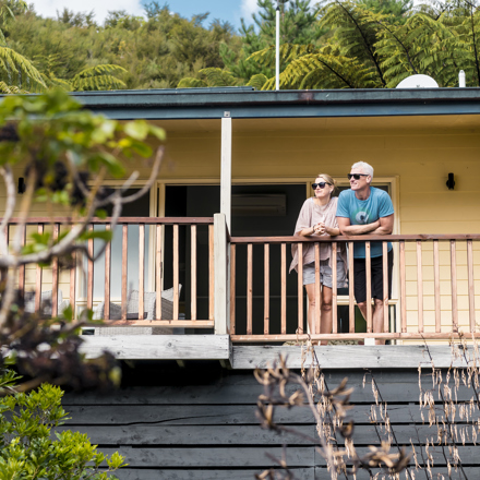Couple admire scenic Endeavour Inlet views from their Fern Studio balcony at Punga Cove surrounded by Punga ferns in the Marlborough Sounds of New Zealand