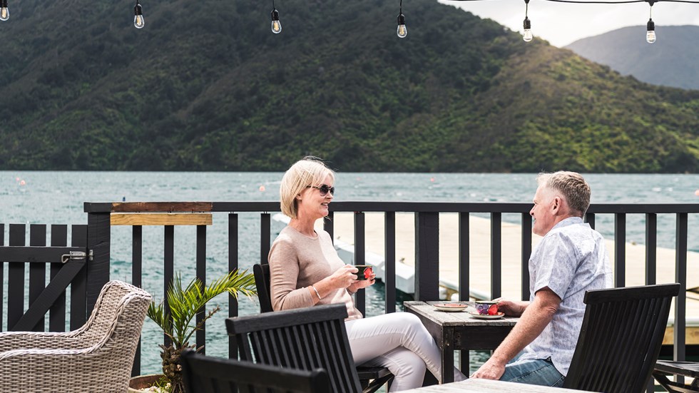 A couple enjoy their coffee at Punga Cove - accompained by views of Endeavour Inlet from the Boatshed Cafe and Bar in New Zealand's South Island Marlborough Sounds