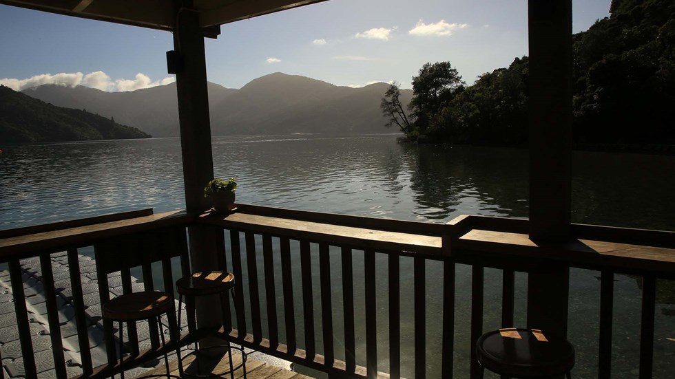 Enjoy an evening drink at the Boatshed Cafe and Bar with a sunset background found at Punga Cove in the New Zealand Marlborough Sounds