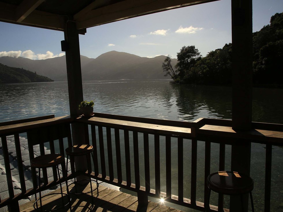 Enjoy an evening drink at the Boatshed Cafe and Bar with a sunset background found at Punga Cove in the New Zealand Marlborough Sounds