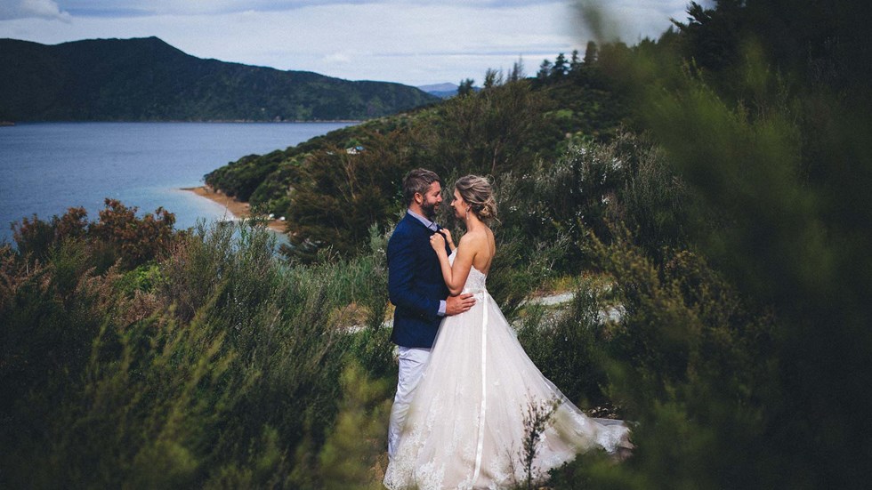 A Bride and Groom face each other on hill above Punga Cove with scenic views of Endeavour Inlet in the background in the Marlborough Sounds of New Zealand