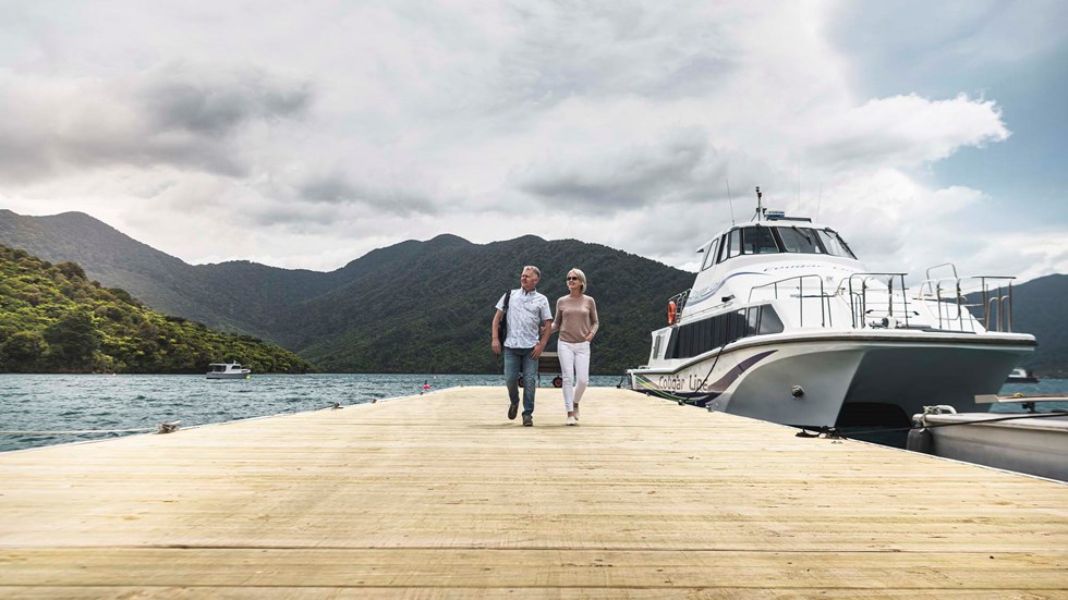 A couple leave Cougar Line vessel from Picton and walk along jetty to Punga Cove in the Marlborough Sounds in New Zealand's top of the South Island